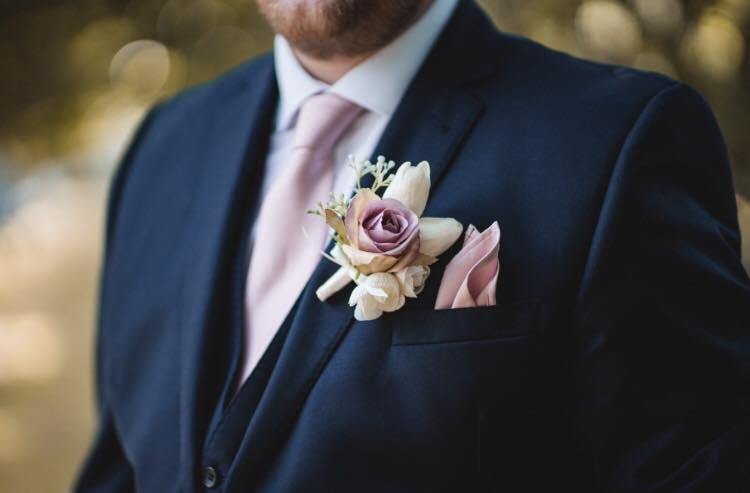 Rose Gold Wedding Tie paired with matching pocket square and boutonniere, worn with a navy suit. Elegant handmade necktie for groomsmen.