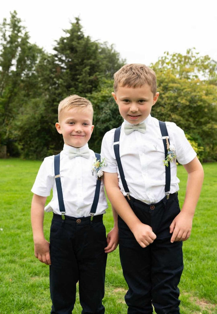 Two boys wearing Willow Bow Ties for Boys in sage green with white shirts and navy suspenders, perfect for wedding party outfits.