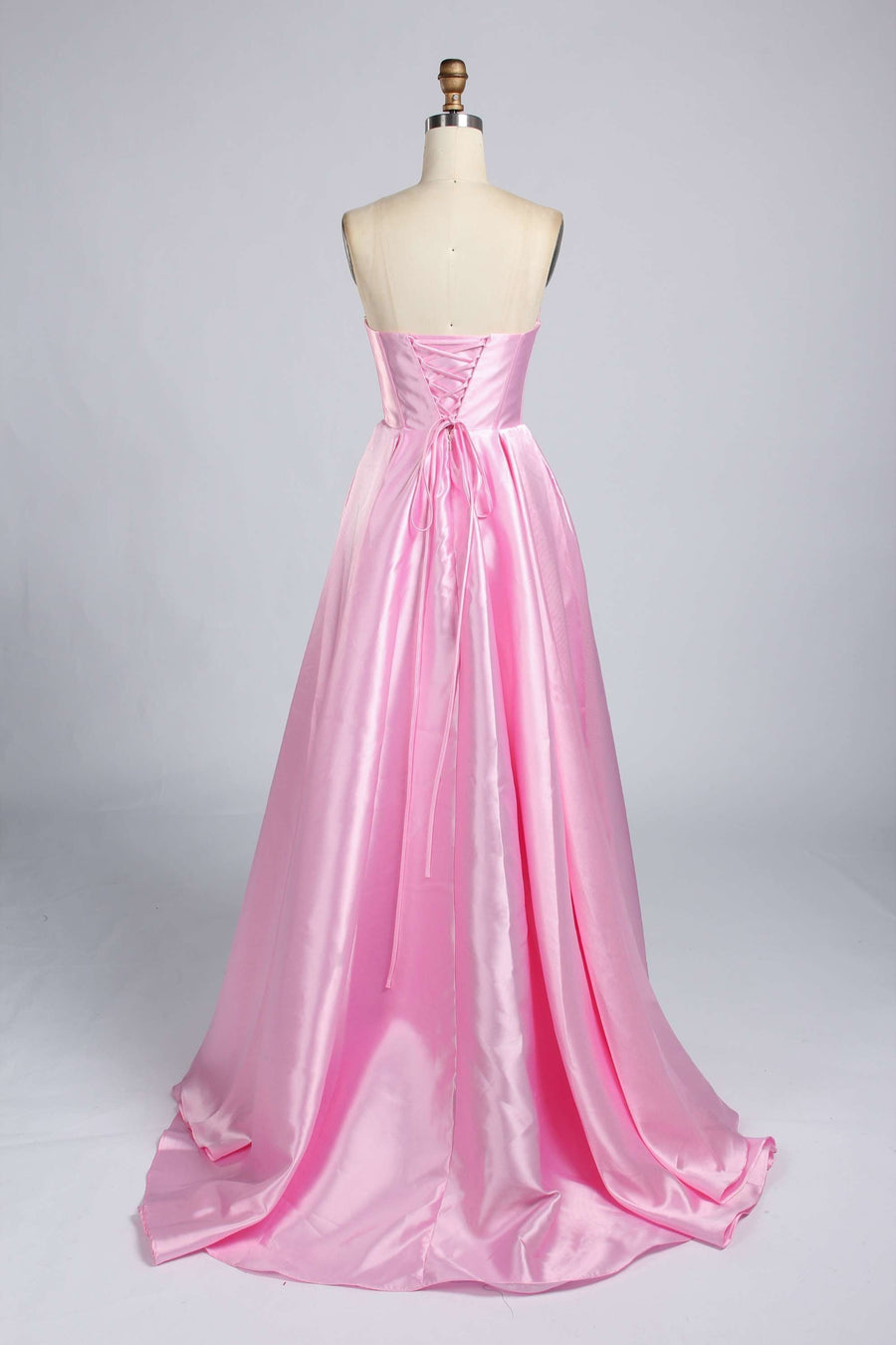 Back view of Carmen Satin Gown with Pockets in elegant pink satin, featuring a lace-up corset and flowing A-line silhouette for formal occasions.