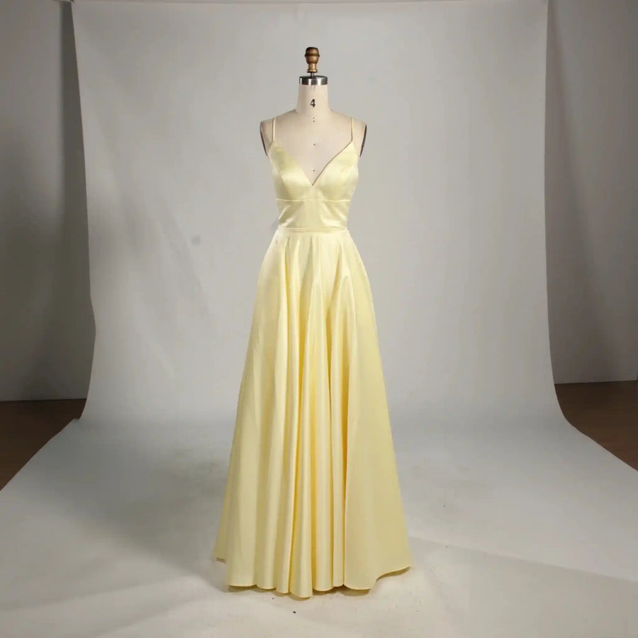 Ava Light Yellow Satin Ballgown with pockets by Jessica Stuart, featuring a deep V-neckline, open back, and full satin skirt for prom or evening wear.
