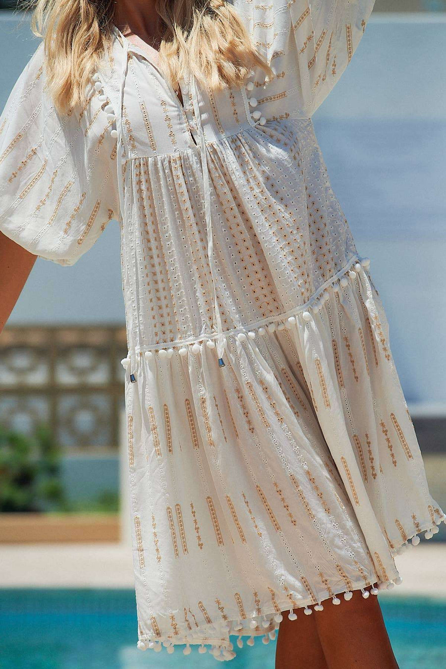 Close-up of Seashell Palace Midi Dress showing pompom trim, tassel ties, and textured fabric with gold detailing. Perfect for summer styling.
