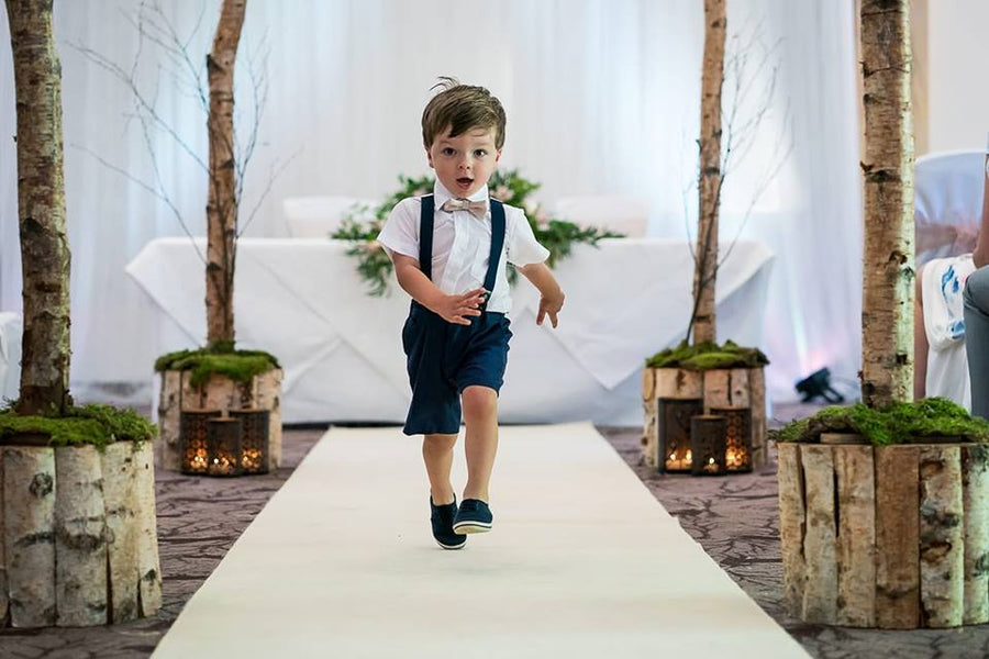 Young boy wearing Blush Pink Boys Bow Tie at a wedding, paired with navy suspenders. Perfect formal accessory for kids aged 5-12.