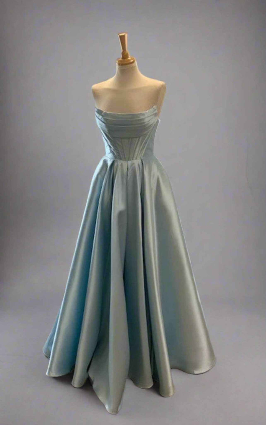 Carmen Ball Gown in light blue satin with strapless neckline, pleated bodice, and full skirt featuring hidden pockets. Ideal for prom or red carpet events.