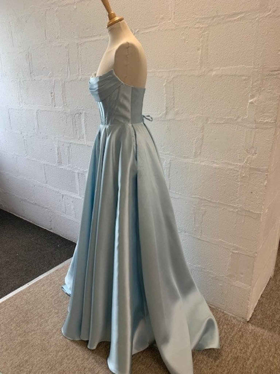 Carmen Ball Gown in light blue satin with strapless neckline, pleated full skirt, and hidden pockets. Elegant formal dress perfect for prom or red carpet.
