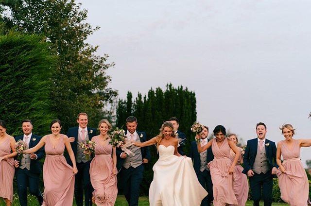 Wedding party running outdoors with bridesmaids in blush dresses and groomsmen wearing Suede Pink Wedding Ties, perfect for coordinated wedding looks.