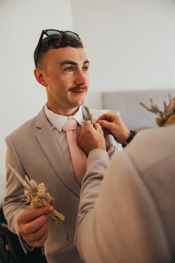 Groom getting ready with Vintage Rose Wedding Tie and boutonniere, highlighting the tie’s soft pink hue and wedding-day elegance.