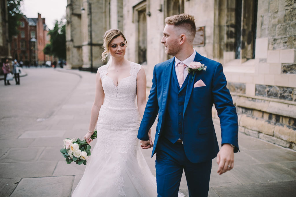 Bride and groom walking hand-in-hand, groom styled in a Vintage Rose Wedding Tie that adds a soft romantic touch to his blue suit.