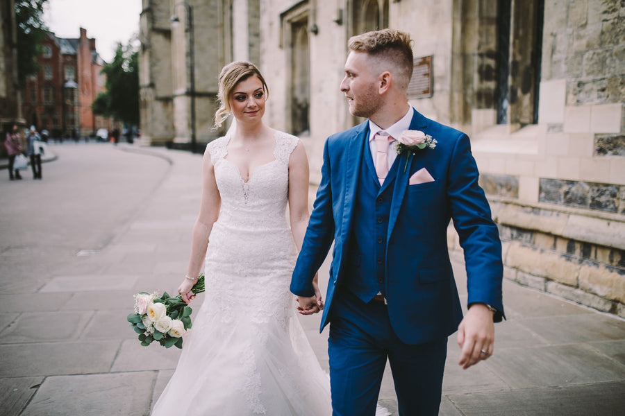 Bride and groom walking hand-in-hand, groom styled in a Vintage Rose Wedding Tie that adds a soft romantic touch to his blue suit.