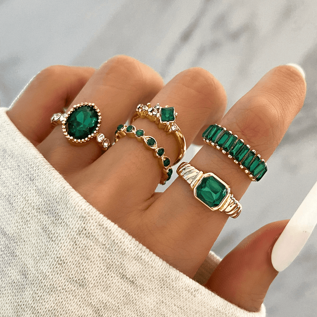 Image of a hand with 5 gold and emerald green rings on various fingers